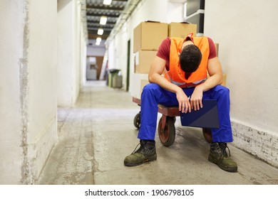 Worker sits exhausted on a push cart in the warehouse because of overtime - Powered by Shutterstock