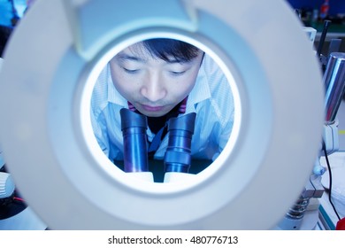 Worker at small parts manufacturing factory in China looking through microscope