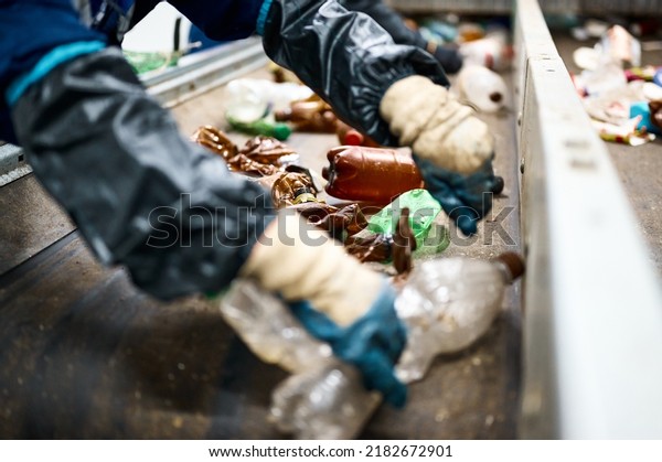 Worker sorts trash on conveyor belt at waste\
recycling plant