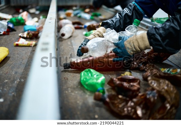 Worker sorts trash on conveyor belt at waste\
recycling plant