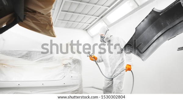Worker\
spraying white paint with spray gun on\
car.
