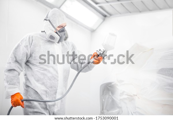Worker\
spraying white paint with spray gun on\
car.
