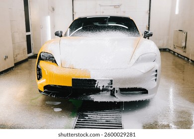 Worker sprays soap solution with high pressure water jet for detailing car wash. Application of soapy foam with high pressure water gun for sports car cleaning at the service