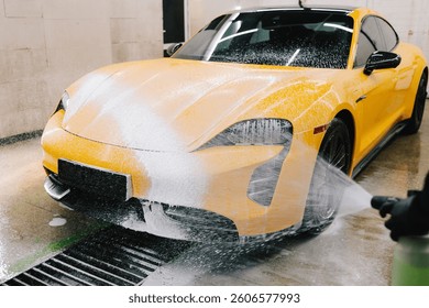Worker sprays soap solution with high pressure water jet for detailing car wash. Application of soapy foam with high pressure water gun for sports car cleaning at the service