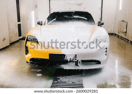 Worker sprays soap solution with high pressure water jet for detailing car wash. Application of soapy foam with high pressure water gun for sports car cleaning at the service