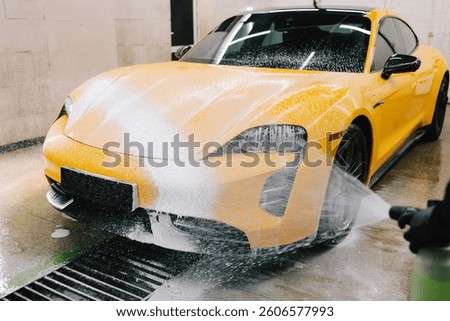 Worker sprays soap solution with high pressure water jet for detailing car wash. Application of soapy foam with high pressure water gun for sports car cleaning at the service