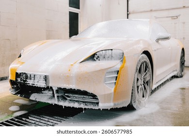 Worker sprays soap solution with pressure from water jet for detailing car wash. Application of soapy foam with a water gun for sports car cleaning at the service