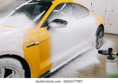 Worker sprays soap solution with pressure from water jet for detailing car wash. Application of soapy foam with a water gun for sports car cleaning at the service