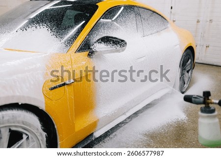 Worker sprays soap solution with pressure from water jet for detailing car wash. Application of soapy foam with a water gun for sports car cleaning at the service