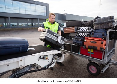 Worker Stacking Luggage On Trailer From Conveyor On Runway