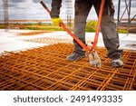 Worker is standing on pile of rusty rectangle steel, reinforcement for concrete as cutting reinforcement grid, mesh with bolt cutters at building site.