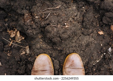 The worker is standing in two brown leather boots against the background of the earth, black soil, soil. Close-up photography, texture, farming, agriculture.
