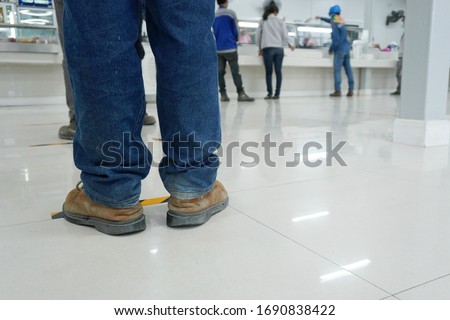 Worker stands before the yellow-black line up to wait to buy food in the factory canteen room during corona virus epidemic. (Covid 19)