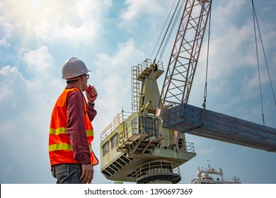 worker stevedore foreman, engineering, loading master talks to crane driver by walkie talkie for safety lifting the goods shipment, lifting by gantry crane, working at risk on the high level insurance