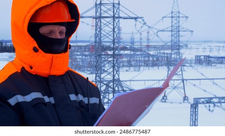 Worker at substation checking documents. Winter conditions highlight complexity and importance of maintaining power supply in cold weather. Ensuring reliable electricity during harsh winter months.