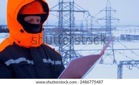 Worker at substation checking documents. Winter conditions highlight complexity and importance of maintaining power supply in cold weather. Ensuring reliable electricity during harsh winter months.