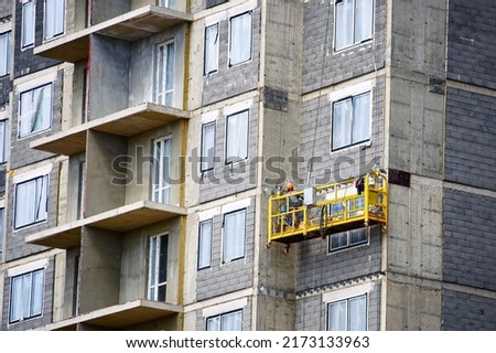 Worker in suspended construction craddle prepare wall facade of hightower residentaial building for insulation and ventilated facade works. Building facades construction works