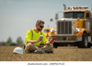 Worker taking break from work drinking coffee and using phone. Builder worker relaxed after work on coffee break. Worker on lunch break. Engineer rest and relax on lunch near construction site.