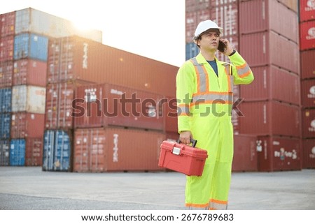 A worker talking on smartphone while holding a toolbox, standing in a container yard