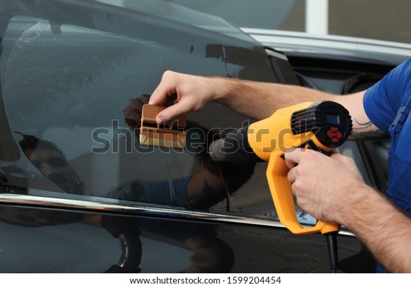 Worker tinting car window with heat gun in\
workshop, closeup