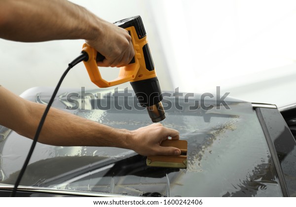 Worker tinting car window with heat gun in\
workshop, closeup