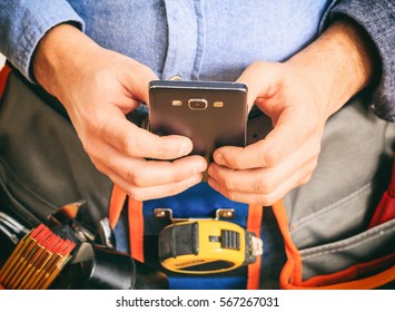 Worker with a tool belt holding a smartphone, closeup view