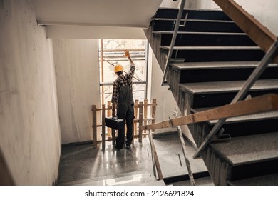 A worker with toolbox in hands looking trough the window in a building at construction process.