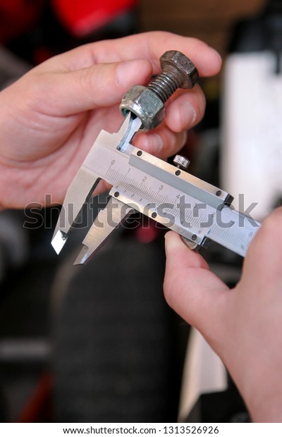 Worker with tools in hands. Mechanic is checking\
and measuring screw size with stainless steel caliper in\
automechanics workshop, car garage. Hands of mechanic holding steel\
screw using steel\
caliper.