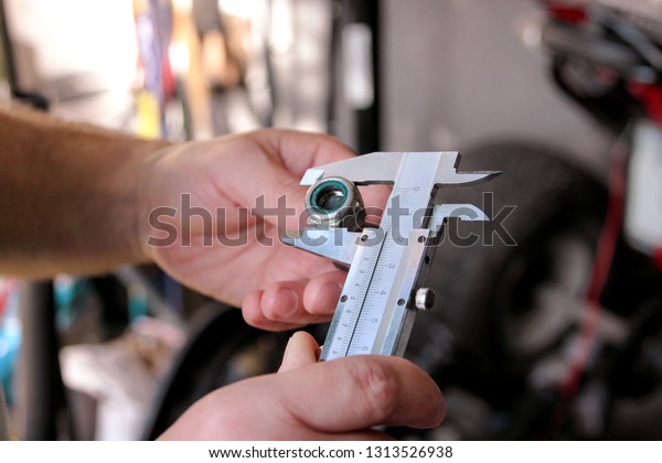 Worker with tools in hands. Mechanic is checking
and measuring screw size with stainless steel caliper in
automechanics workshop, car garage. Hands of mechanic holding steel
screw using steel
caliper.