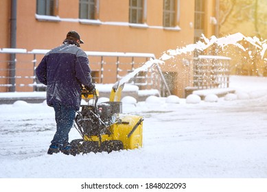 Worker with track drive snow thrower removing deep snow, heavy duty assistant for snow and ice removal in winter season. Motor machine for removing deep, wet, heavy snow. Snowblower equipment