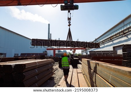 Worker transporting stack of metal pipes with gantry crane in the steel factory