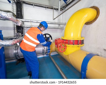 Worker Turning Wheel Of Valve In Industrial Factory. Employee In An Orange Warning Vest Controls A Sludge Pipe Valve. 