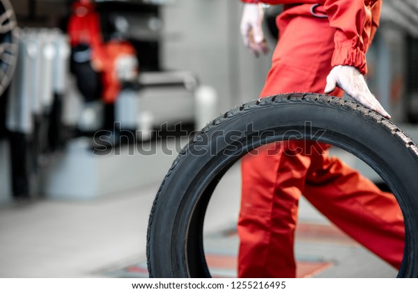 Worker in uniform carrying new tires at the car\
service or store, close-up\
view