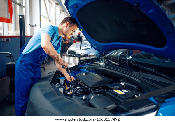 Worker in uniform\
checks engine, car\
service
