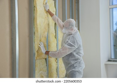 Worker in uniform and respiratory mask insulating wall indoors