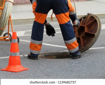 Worker in uniform stand over the open sewer hatch. Repair of sewage or underground utilities, nightman cleans drains, cable laying
