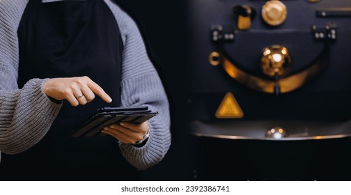 Worker use computer tablet for checks quality on professional mixing roaster machine, process roasting coffee beans. Banner food industry.
