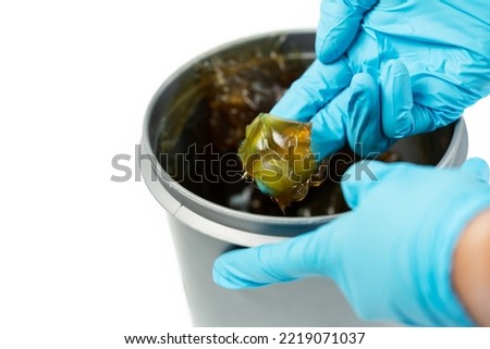 Worker use finger with glove to scoop up lithium grease from white plastic can in the laboratory. Yellow transparance grease on the finger. Testing and manufacturing concept