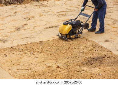 Worker in use vibratory plate compactor for path construction. Plate compactor for compaction sand. Industrial equipment with a combustion engine.