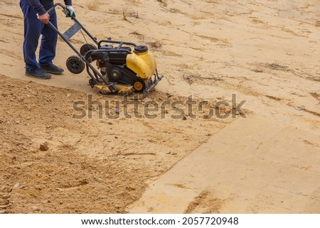 Worker in use vibratory plate compactor for path construction. Plate compactor for compaction sand. Industrial equipment with a combustion engine.