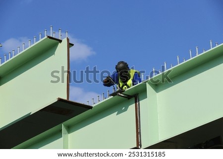 A worker use a welding machine to weld a large and heavy metal section of a bridge under construction.
