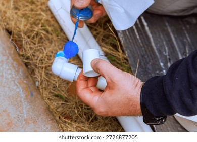 Worker uses glue to attach two pieces of plastic pipe while crouched on ground