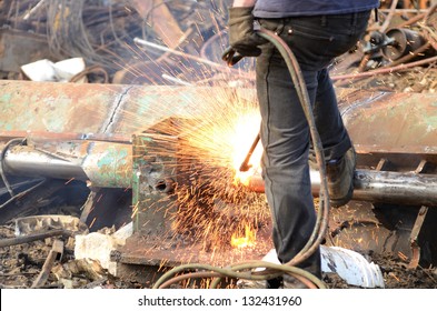 A worker uses a oxygen acetylene cutting torch to cut a large metal object into manageable pieces at a metal recycling plant