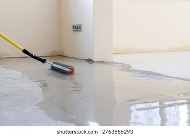 A worker uses a roller to apply epoxy coating on a newly poured concrete floor. The space is undergoing renovation in the afternoon light. Roller for self-leveling floor.