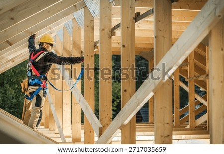 A worker uses safety gear while climbing wooden beams on a construction site during daytime hours.