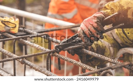 A worker uses steel tying wire to fasten steel rods to reinforcement bars close-up. Reinforced concrete structures - making a steel reinforcing cage for concrete beam