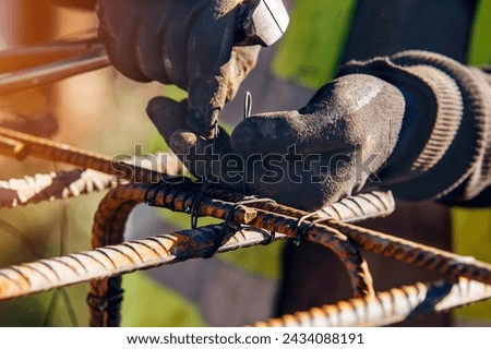 A worker uses steel tying wire to fasten steel rods to reinforcement bars close-up. Reinforced concrete structures - making a steel reinforcing cage for a concrete beam