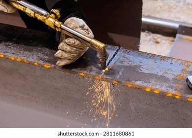Worker uses torch to weld two pieces of metal together in workshop sparks fly as metal heats up.