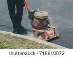 Worker uses vibratory plate compactor compacting asphalt at road repair