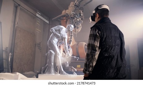 A worker uses a VR technology augmented reality holographic interface to visualize a 3D sculpture model project for a robotic milling machine arm in workshop